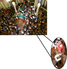 A person in a peach dress and another person in a gray hat and white shirt in a small photo with arrows pointing to where they are standing in a larger photo of over 1000 people at a rally at the Pennsylvania Capitol.