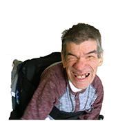 A smiling person with gray hair wearing a gray shirt with red sleeves, using a wheelchair.