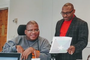Two smiling people, one in a wheelchair, the other standing, going over some paperwork.
