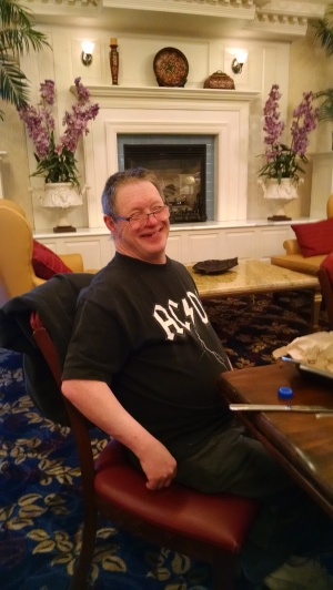 A smiling person sitting at a table in a hotel lobby near a fireplace.