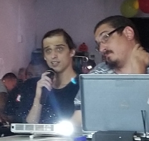 A person holding a microphone reads from a projector screen while another person looks on.