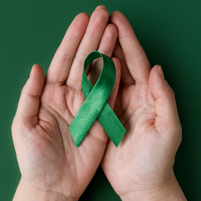 A pair of hands holding a green awareness ribbon in front of a matching green background