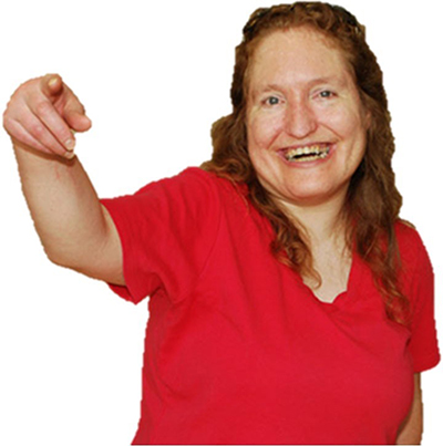 A smiling person with long red hair wearing a red shirt and pointing.