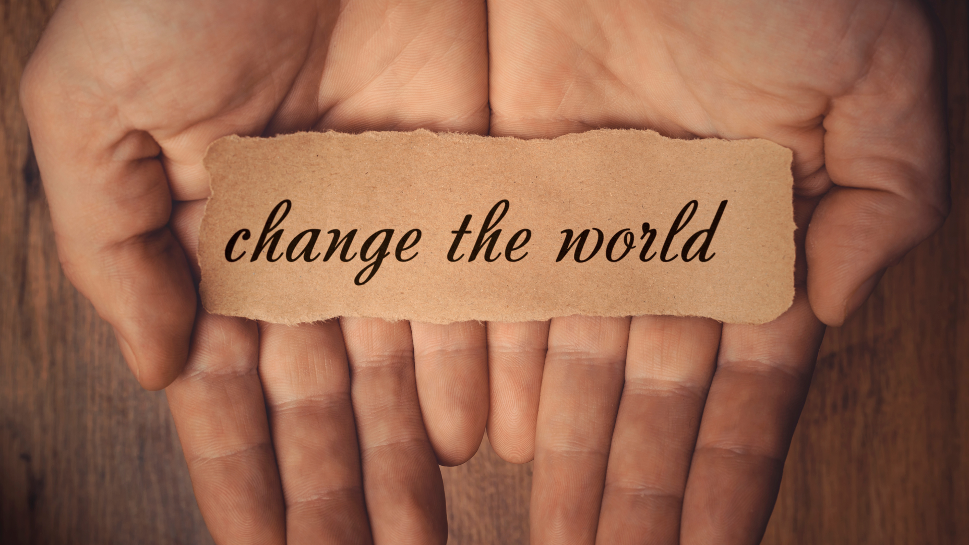 Hands holding a piece of paper that says change the world.